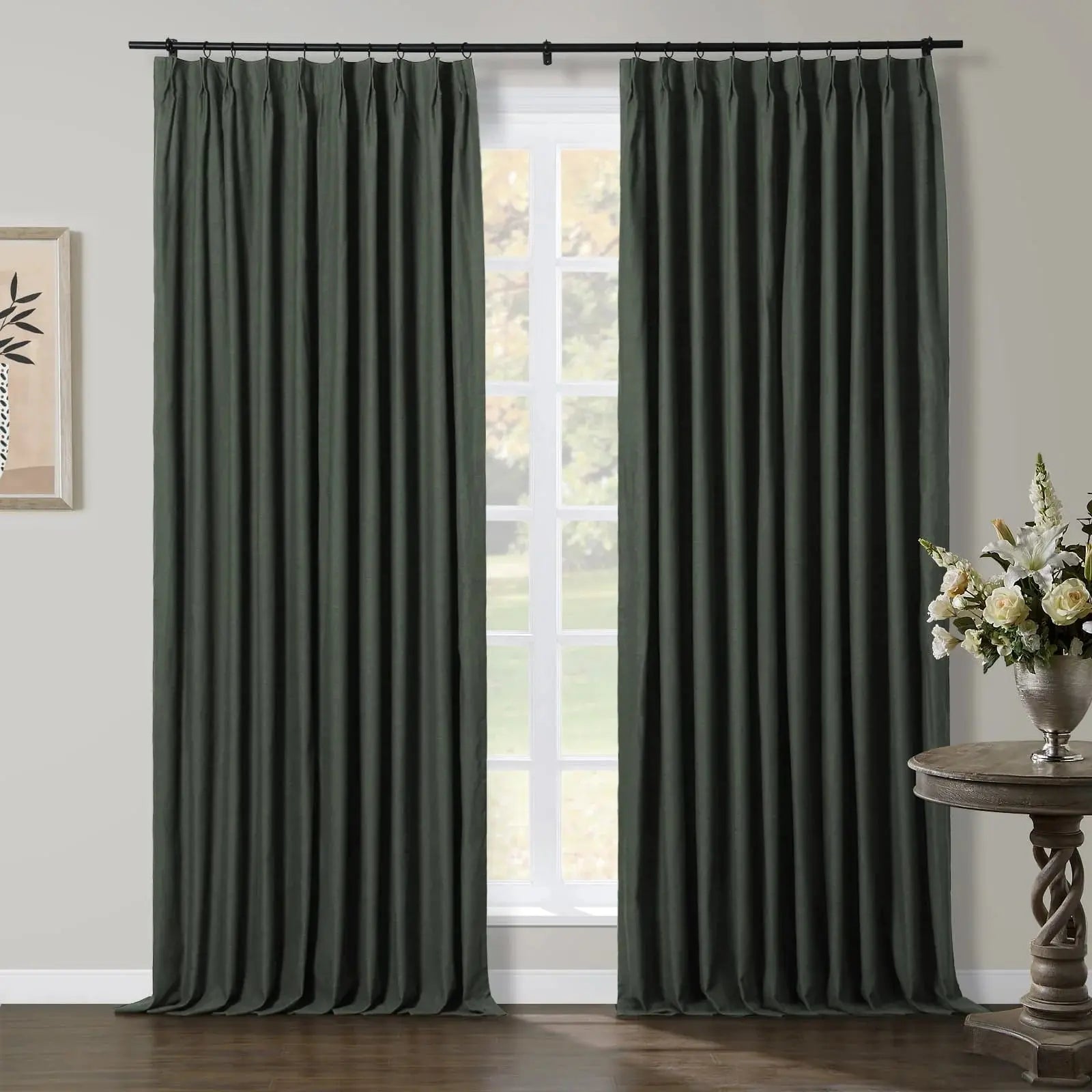 Dark green pinch-pleat curtains adorning a sunlit window in a contemporary room, featuring a carved wooden side table with a white flower arrangement and minimalist wall art