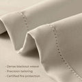 Photograph of light beige blackout curtain fabric showcasing a dense weave, precision tailoring with fine visible stitching, and certified fire protection features