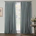 Teal blue pinch pleat linen curtains framing a white paned window in a domestic setting with a dark wood floor a distressed wood side table holding a silver vase with white and cream flowers and a framed botanical art print