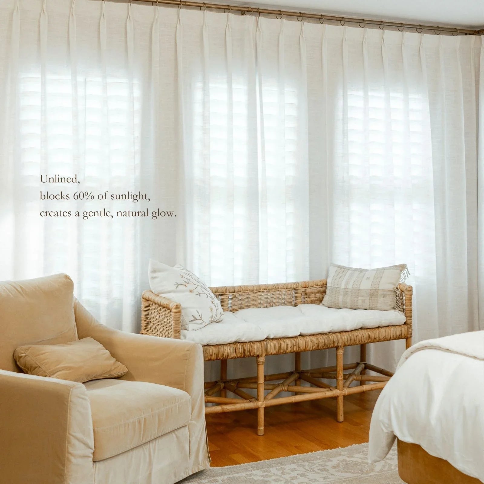A serene room interior with sheer white linen curtains on a gold rod blocking 60% of sunlight for a natural glow, a woven rattan bench featuring a white cushion and a floral embroidered pillow, and a cream slipcovered armchair