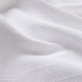 Close-up photograph of white textured fabric displaying gentle folds subtle shadows and a fine linen-like weave