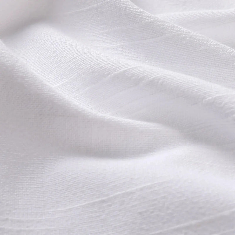 Close-up photograph of white textured fabric displaying gentle folds subtle shadows and a fine linen-like weave
