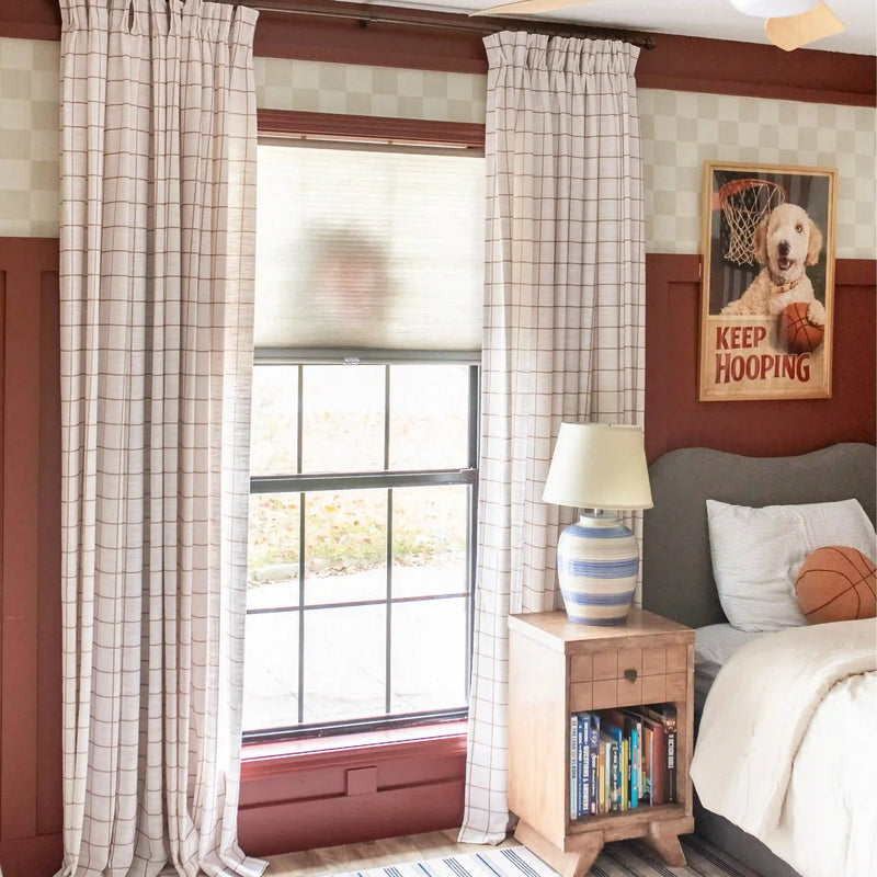 Bedroom with plaid curtains, nightstand, lamp, and sports-themed decor.