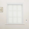 A window in an interior room showcasing white zebra Blinds, accompanied by a small framed botanical art print on the left and a white remote control on the right wall