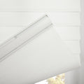 White textured fabric Roman Blind with visible top mounting track unfurling, revealing a layered design and outdoor green foliage