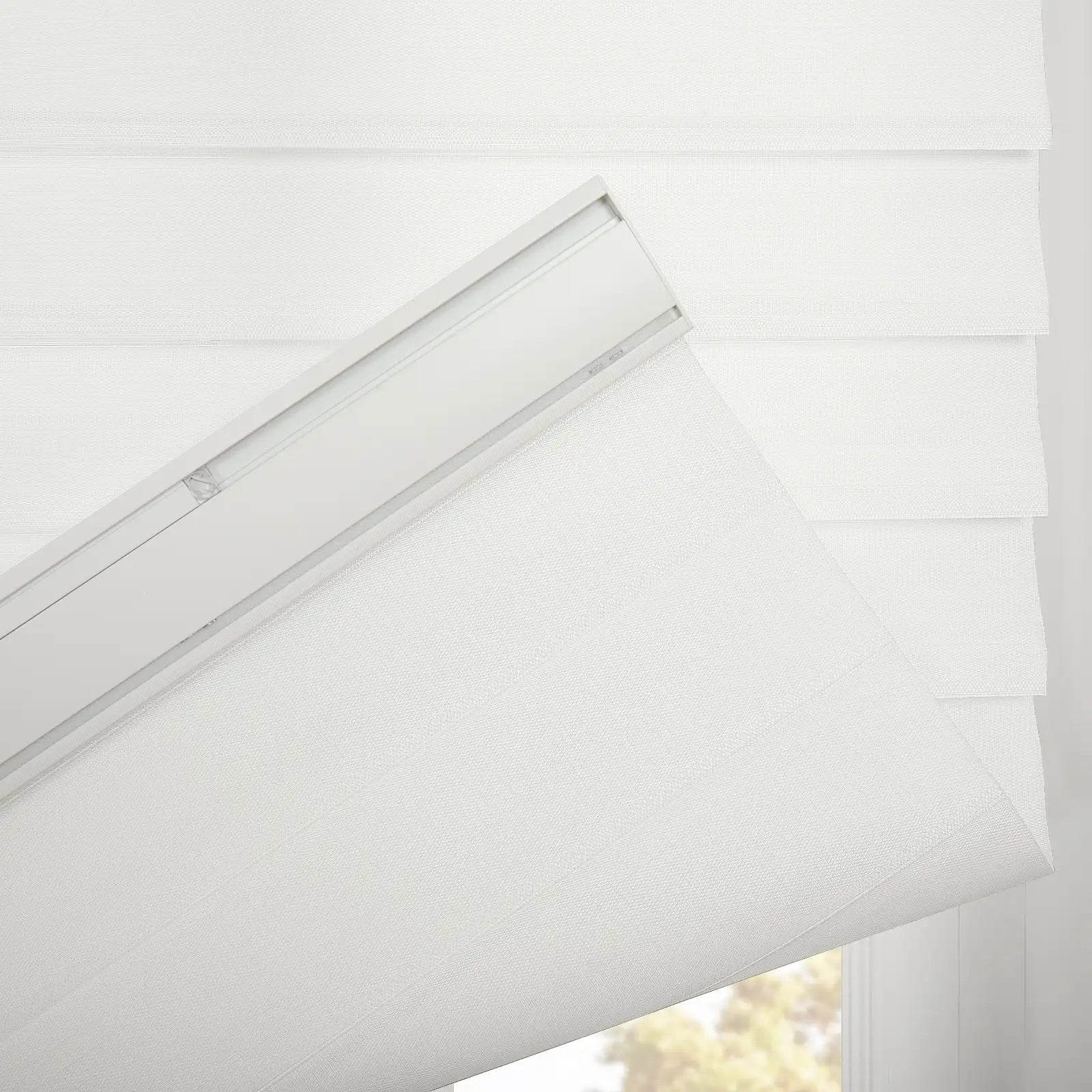 White textured fabric Roman Blind with visible top mounting track unfurling, revealing a layered design and outdoor green foliage