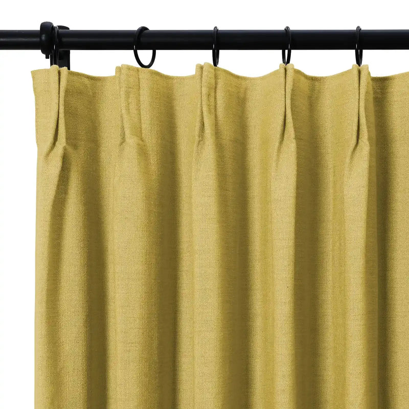 Chartreuse green woven fabric curtain with a pinch pleat top hanging from a black rod with dark rings showcasing soft vertical folds