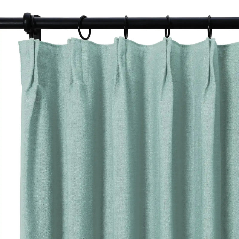 Light teal woven curtain with a pleated header hanging from black rings on a black rod
