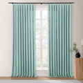 Aqua pinch pleat curtains on a black rod in a contemporary room, featuring textured fabric, a prominent grid window, and a fluted wooden side table with a black vase holding greenery