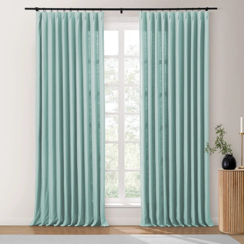 Aqua pinch pleat curtains on a black rod in a contemporary room, featuring textured fabric, a prominent grid window, and a fluted wooden side table with a black vase holding greenery