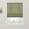 Roman blind featuring a muted green background with a delicate dark green leafy vine pattern partially drawn over a window offering a blurred view of trees, a framed rustic landscape painting hangs nearby