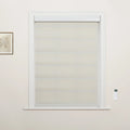 A light beige layered fabric window Blind covers a white-trimmed window, featuring a white wall-mounted remote control on the right and a framed botanical sketch on the left