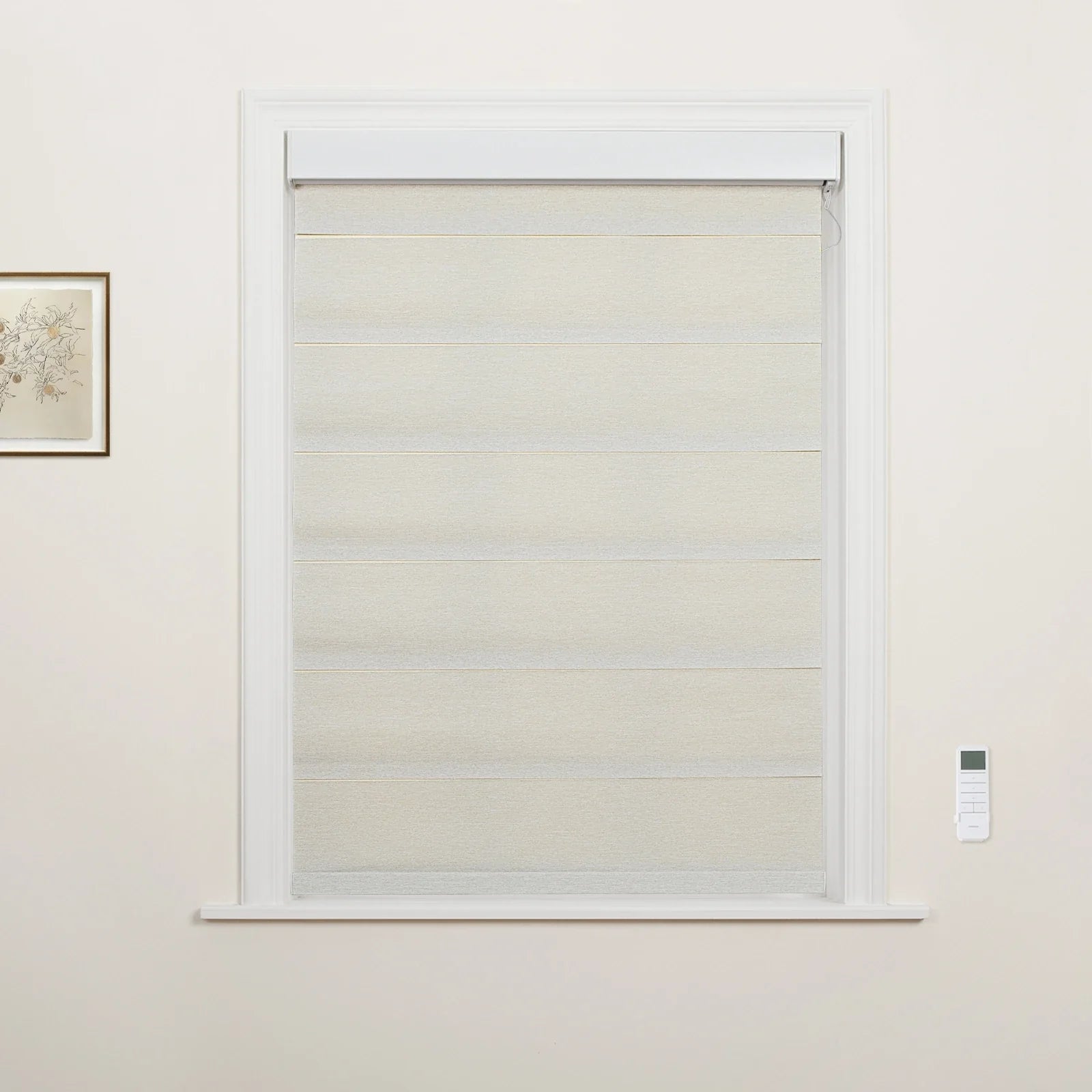 A light beige layered fabric window Blind covers a white-trimmed window, featuring a white wall-mounted remote control on the right and a framed botanical sketch on the left