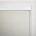 A close-up of a beige textured window Blind with subtle horizontal banding, a white headrail, and classic white decorative window trim, featuring a slender control cord visible on the right