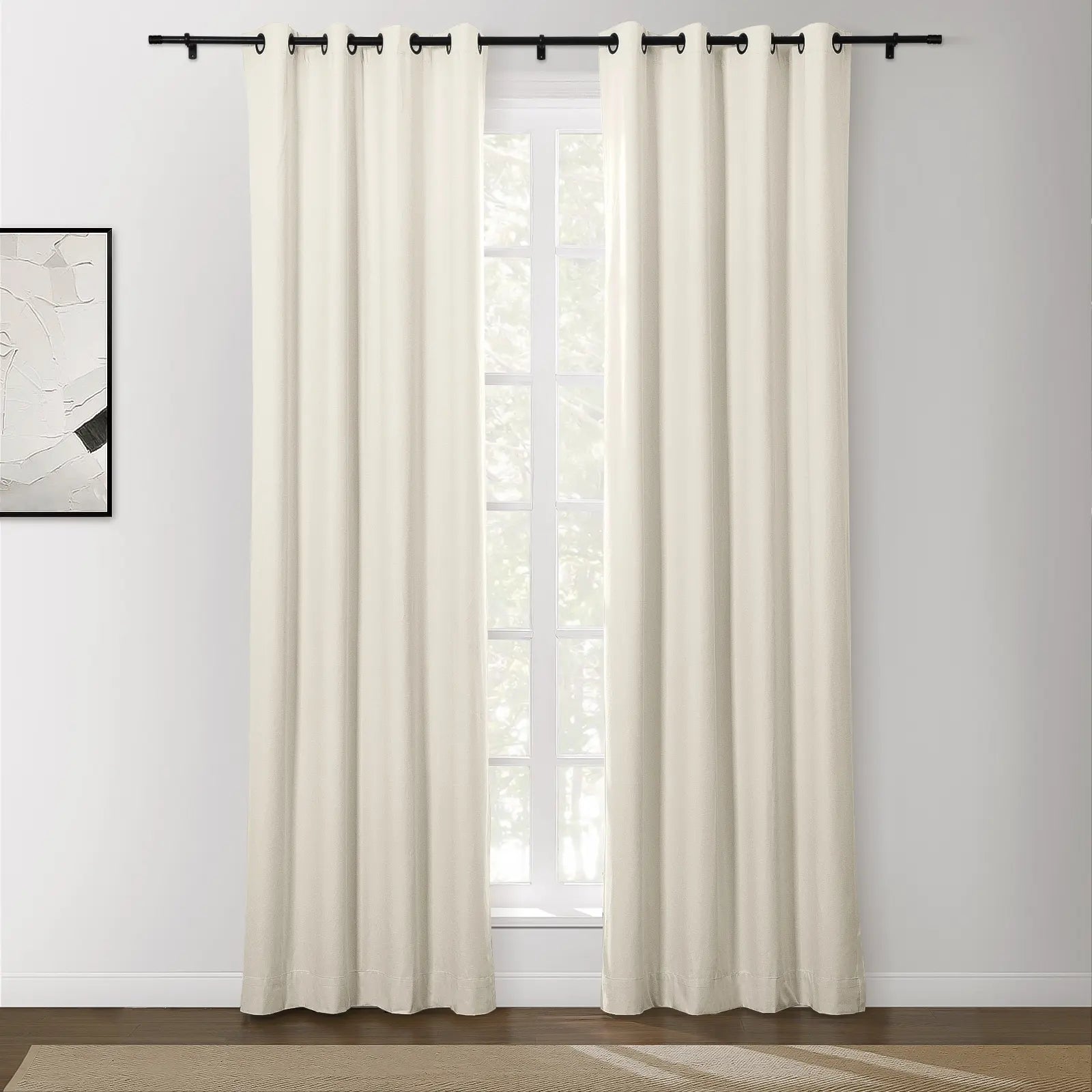 Photograph of cream-colored blackout curtains with black grommet tops on a black rod in a modern room featuring an abstract wall painting
