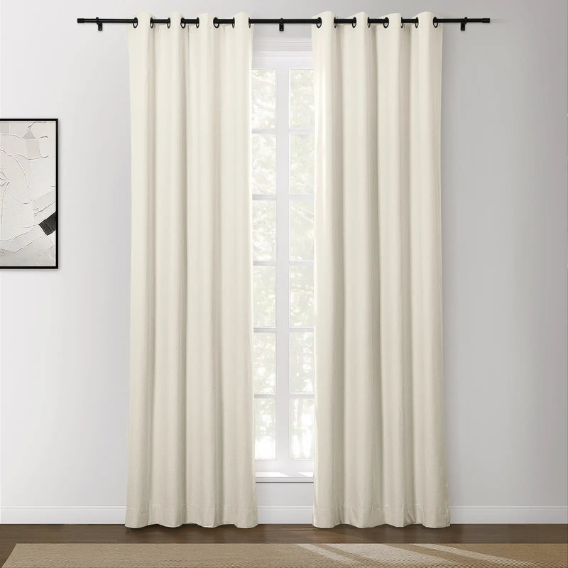 Photograph of cream-colored blackout curtains with black grommet tops on a black rod in a modern room featuring an abstract wall painting