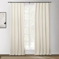 Cream blackout curtains on a black rod flank a large window overlooking trees, with a modern abstract painting on the left wall and a beige textured rug on the wood floor