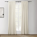 Photograph of a modern living room featuring off-white pinch-pleat drapes on a black rod framing a window with white grilles an abstract white and black artwork on the wall and a dark wood floor with a beige chevron rug
