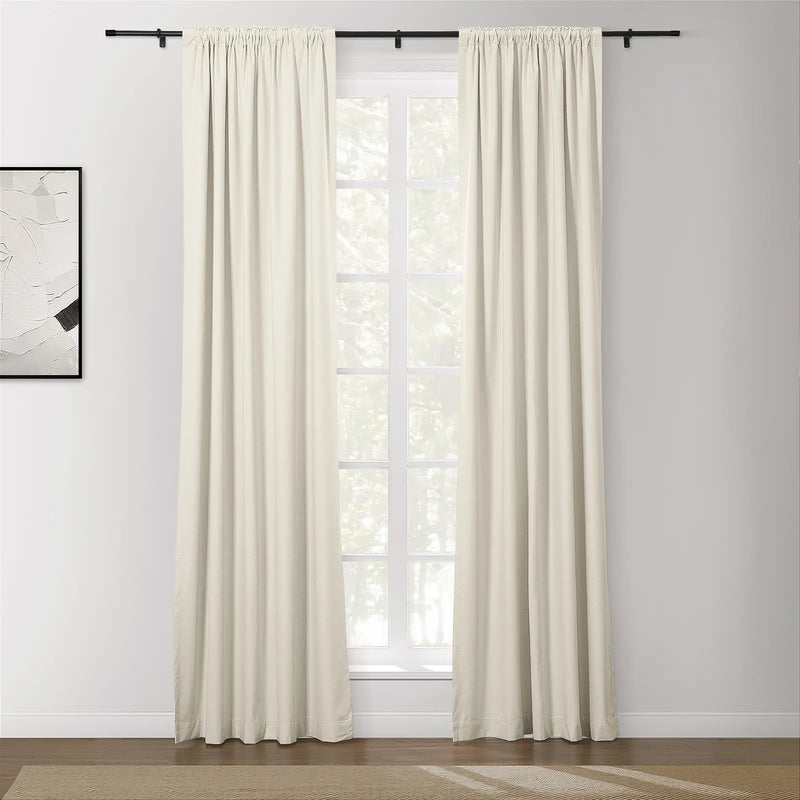 Photograph of a modern living room featuring off-white pinch-pleat drapes on a black rod framing a window with white grilles an abstract white and black artwork on the wall and a dark wood floor with a beige chevron rug