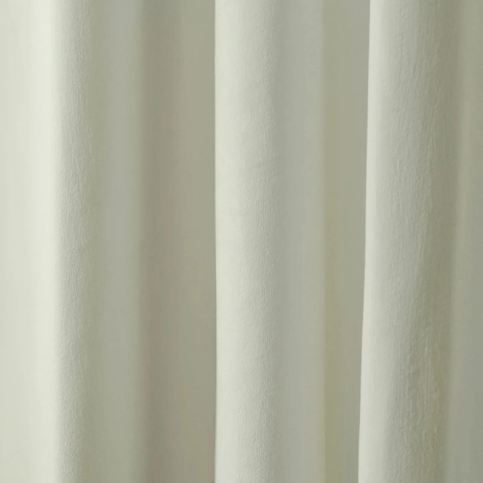 Photograph of a creamy off-white textured fabric curtain featuring soft vertical folds and subtle light and shadow interplay