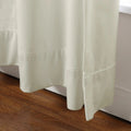 Off-white textured curtains with prominent stitched hems and soft folds pooling near a warm brown wood floor