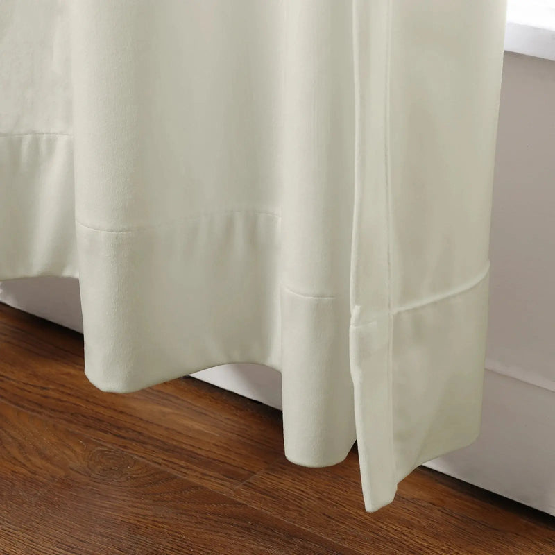 Off-white textured curtains with prominent stitched hems and soft folds pooling near a warm brown wood floor