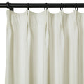 Off-white pleated fabric curtain hanging from black rings on a sleek black metal rod against a clean white background