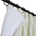 Close-up of white and cream pleated curtains hanging from a black curtain rod with black rings, one white panel pulled back revealing a small white plastic hook