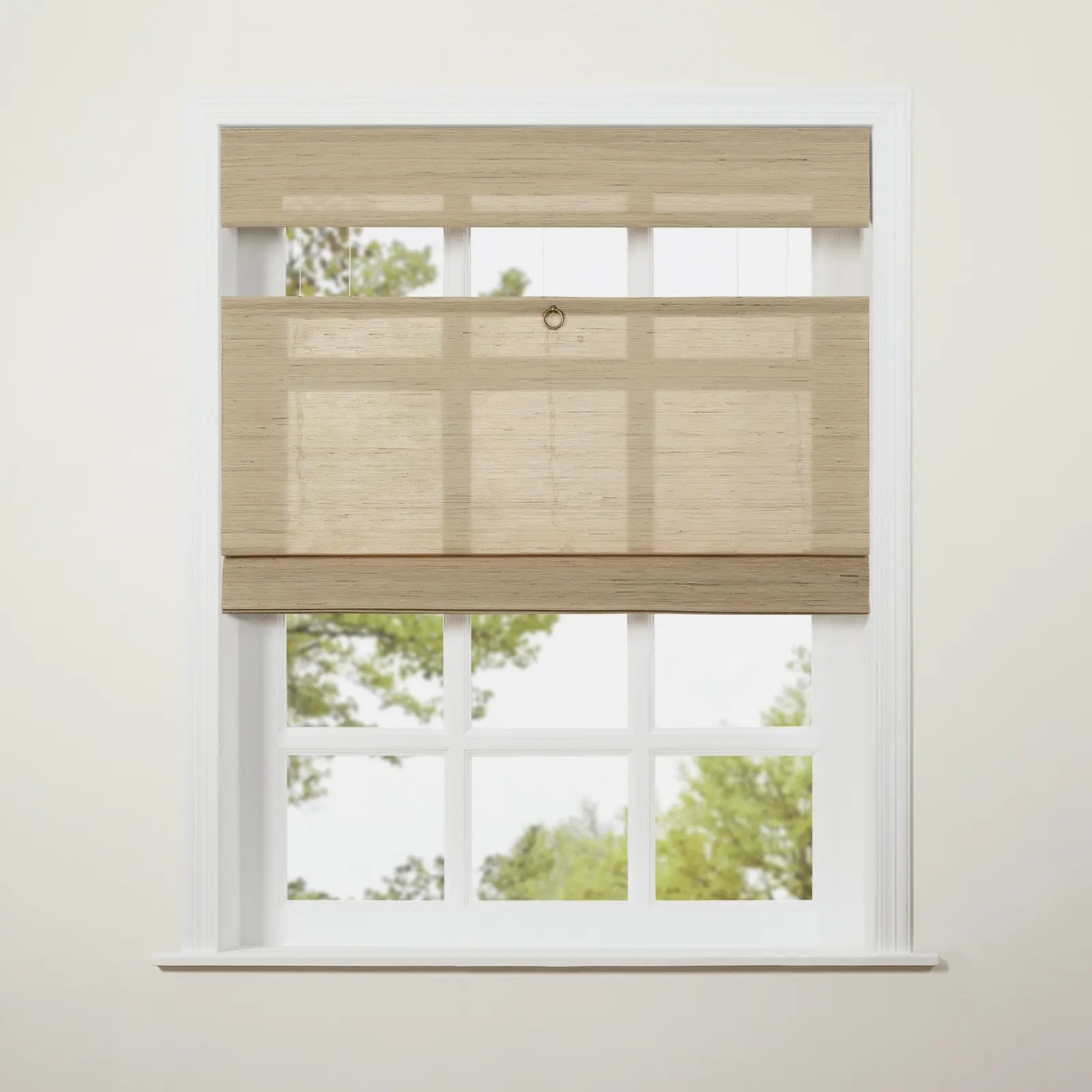Photograph of a light beige textured woven top-down bottom-up roman blind with a bronze ring pull covering a white multi-pane window with green trees visible outside