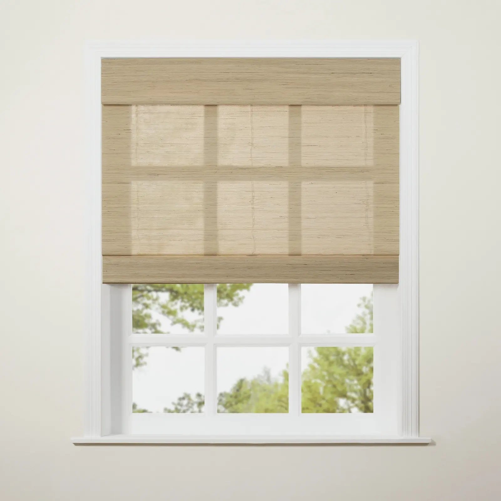 A light beige textured Roman blind partially drawn over a white six-pane window revealing blurred green trees and bright sky outside