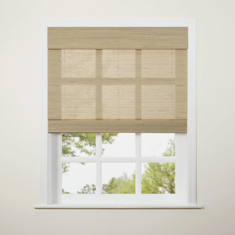 A light beige textured Roman blind partially drawn over a white six-pane window revealing blurred green trees and bright sky outside