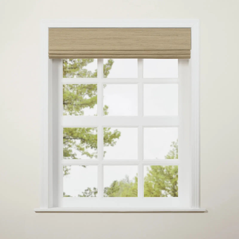 Photograph of a white multi-pane window featuring a tan woven Roman blind, set against an off-white wall with blurry green trees visible outside
