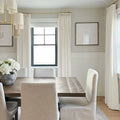 Neutral contemporary dining room featuring a dark wood dining table, light upholstered chairs, a grey vase with white hydrangeas, and a modern gold chandelier against textured wallpaper