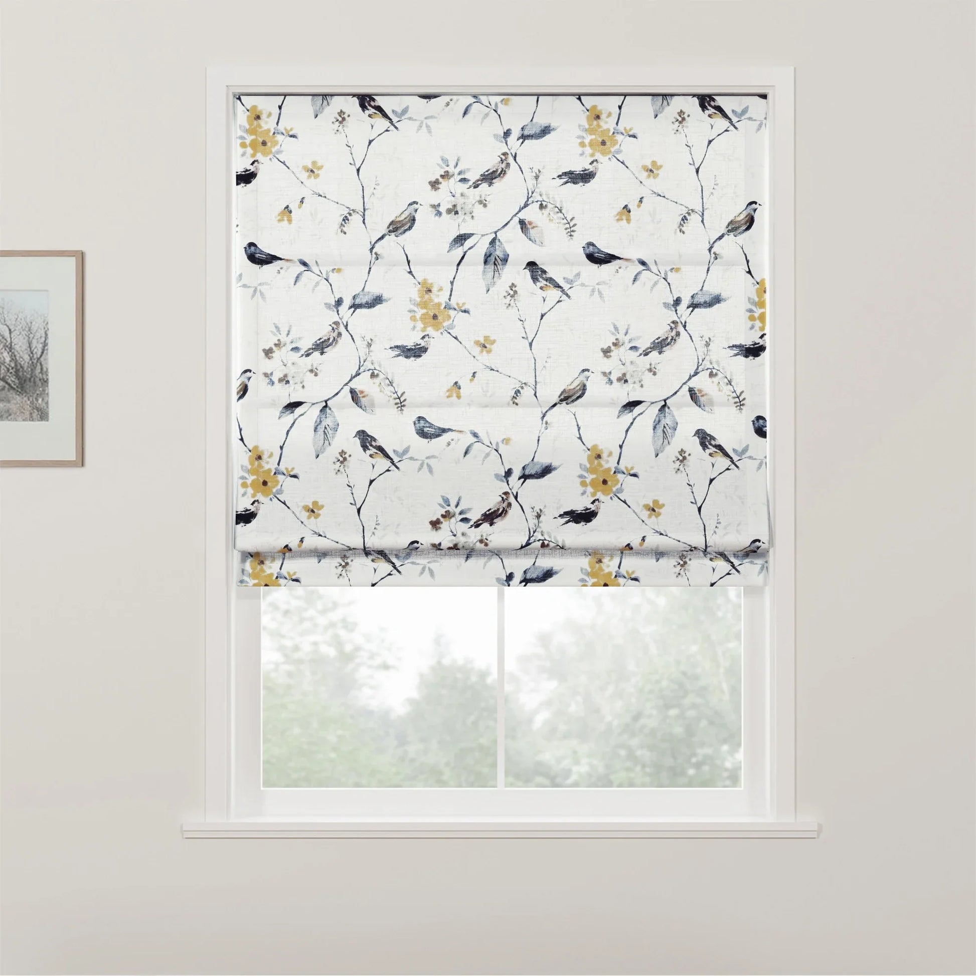 Photograph of a white Roman blind with an intricate pattern of birds perched on branches featuring yellow flowers and blue leaves, covering a window that looks out onto blurred greenery