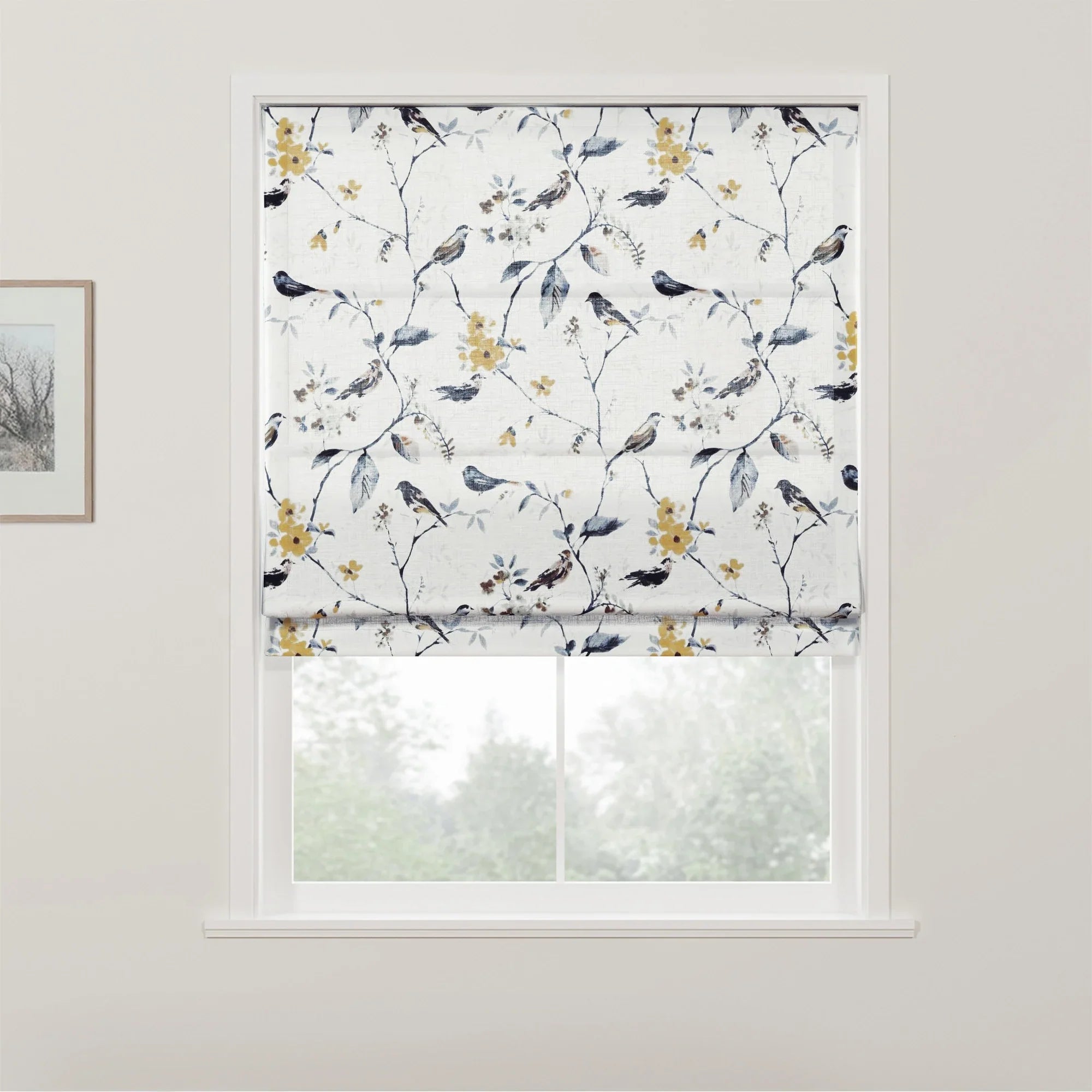Photograph of a white Roman blind with an intricate pattern of birds perched on branches featuring yellow flowers and blue leaves, covering a window that looks out onto blurred greenery