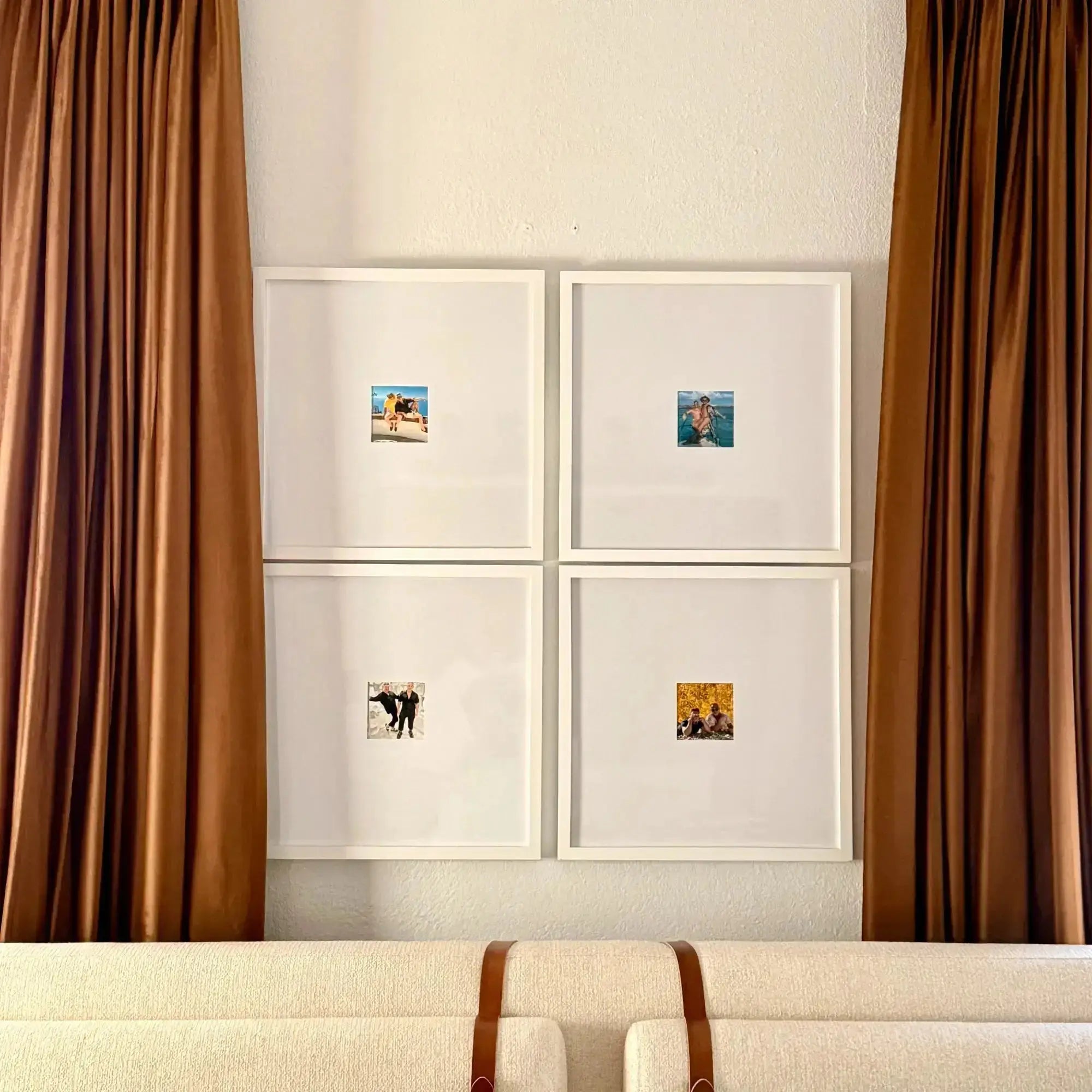 A gallery wall with four small framed personal photos showcasing candid moments, framed by lush brown velvet curtains and resting above a cream textured sofa with brown leather straps