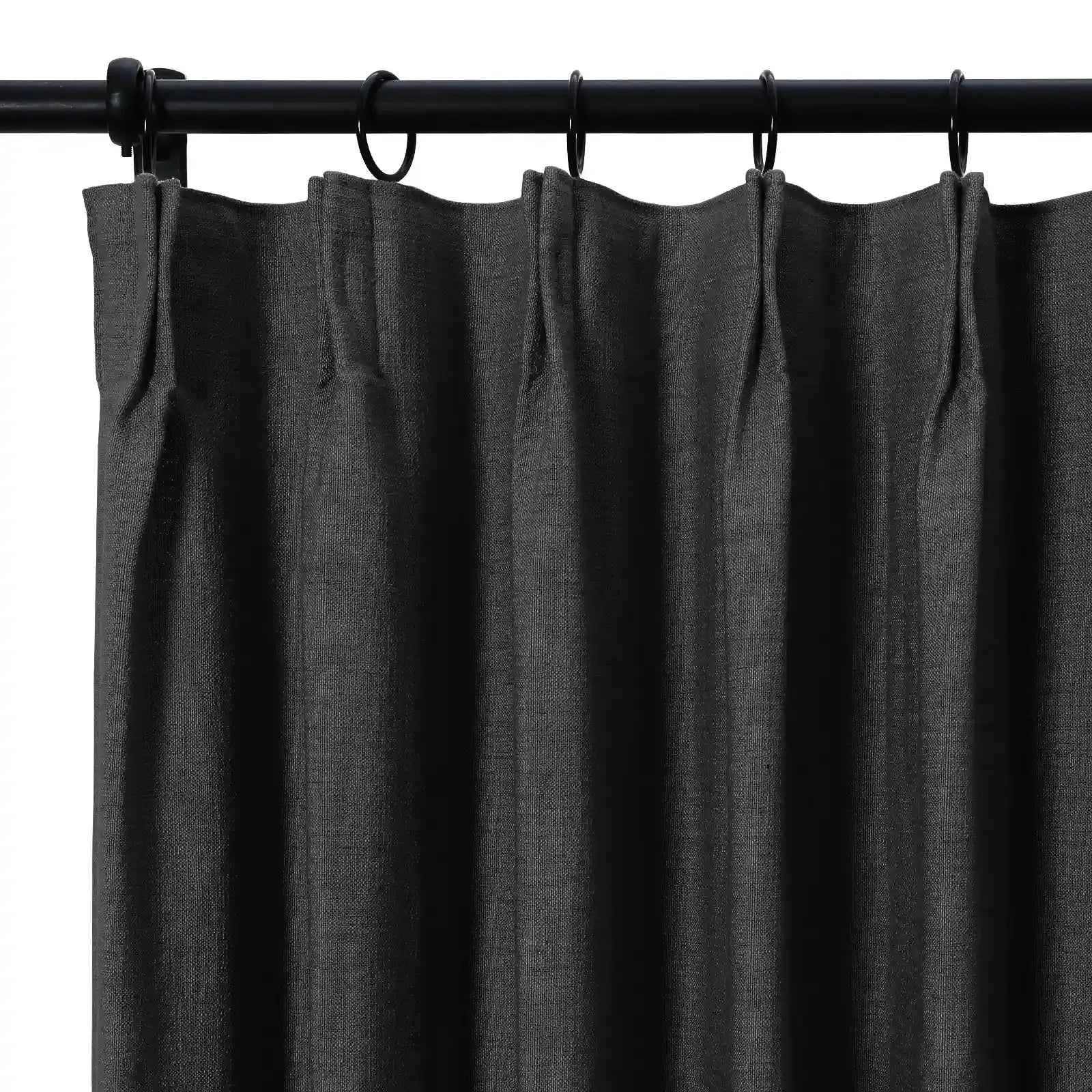Dark charcoal linen-textured curtain with precise pleats hanging from a matte black rod and rings