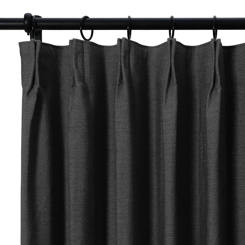 Dark charcoal linen-textured curtain with precise pleats hanging from a matte black rod and rings