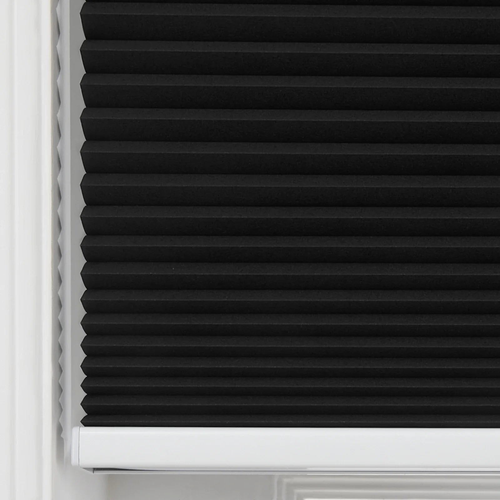 Close-up of a black cellular Blind featuring sharp horizontal pleats, neatly installed within a white window frame with a visible white bottom rail