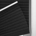 Close-up of a black pleated cellular Blind with a distinct accordion texture and white top rail at a window