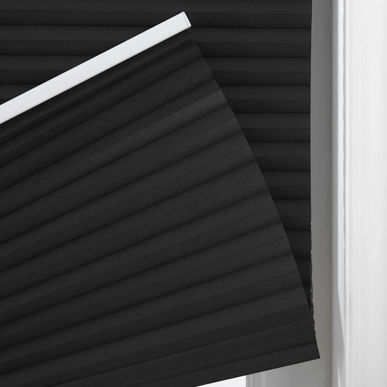 Close-up of a black pleated cellular Blind with a distinct accordion texture and white top rail at a window