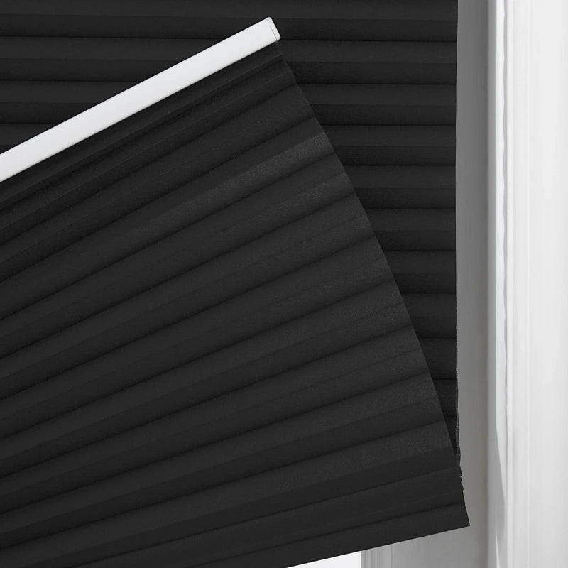 Close-up of a black pleated cellular Blind with a distinct accordion texture and white top rail at a window