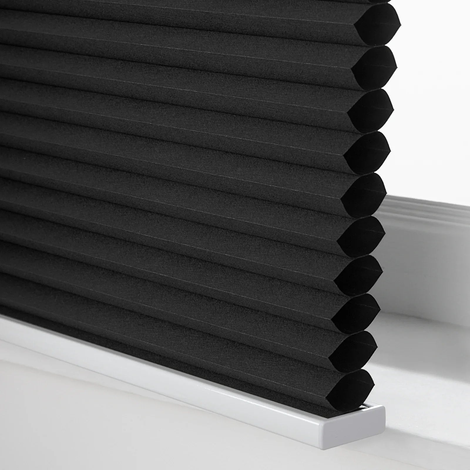 Photograph of black cellular Blinds with a textured honeycomb fabric and a crisp white bottom rail on a window