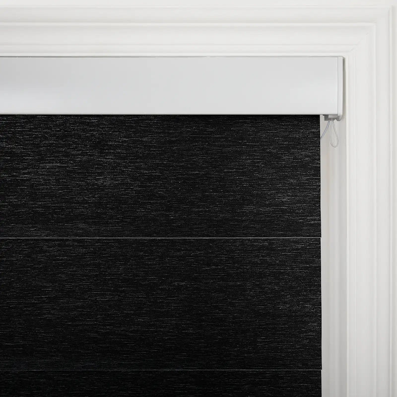 Close-up of a black textured fabric layered window Blind with a white headrail and a classic white molded window frame in an interior setting revealing the control cord