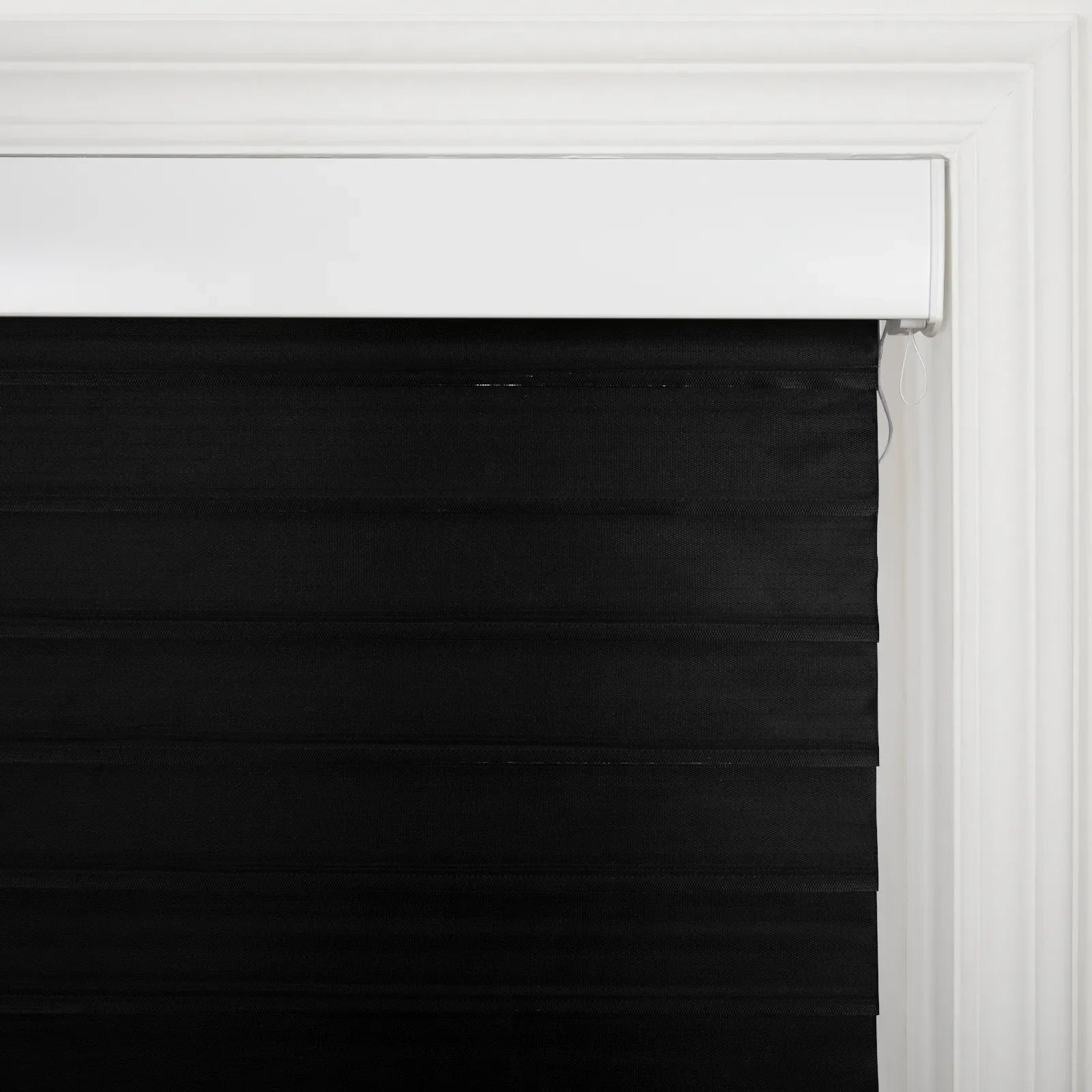 Black horizontal fabric window Blinds featuring a white headrail and decorative white trim around the frame with a visible white pull cord on the right side