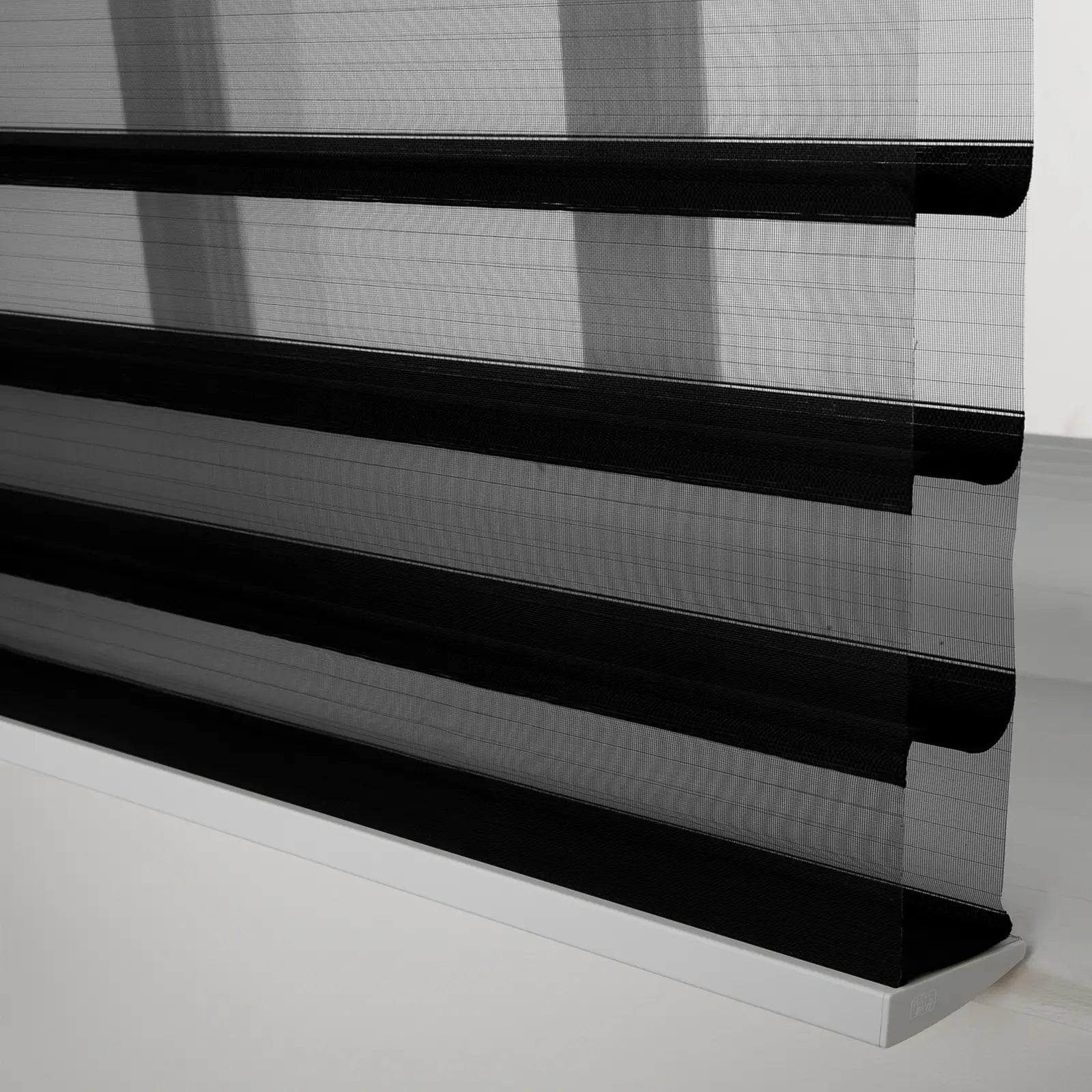 Close-up of modern zebra roller Blinds with alternating black opaque and sheer mesh horizontal stripes resting on a white bottom rail