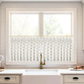 A kitchen window with a white cafe curtain featuring a golden teardrop pattern above a white farmhouse sink with a brass faucet and subway tile backsplash