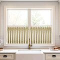 A kitchen window featuring pleated beige cafe curtains with a white leaf pattern, an antique brass faucet, and a white farmhouse sink