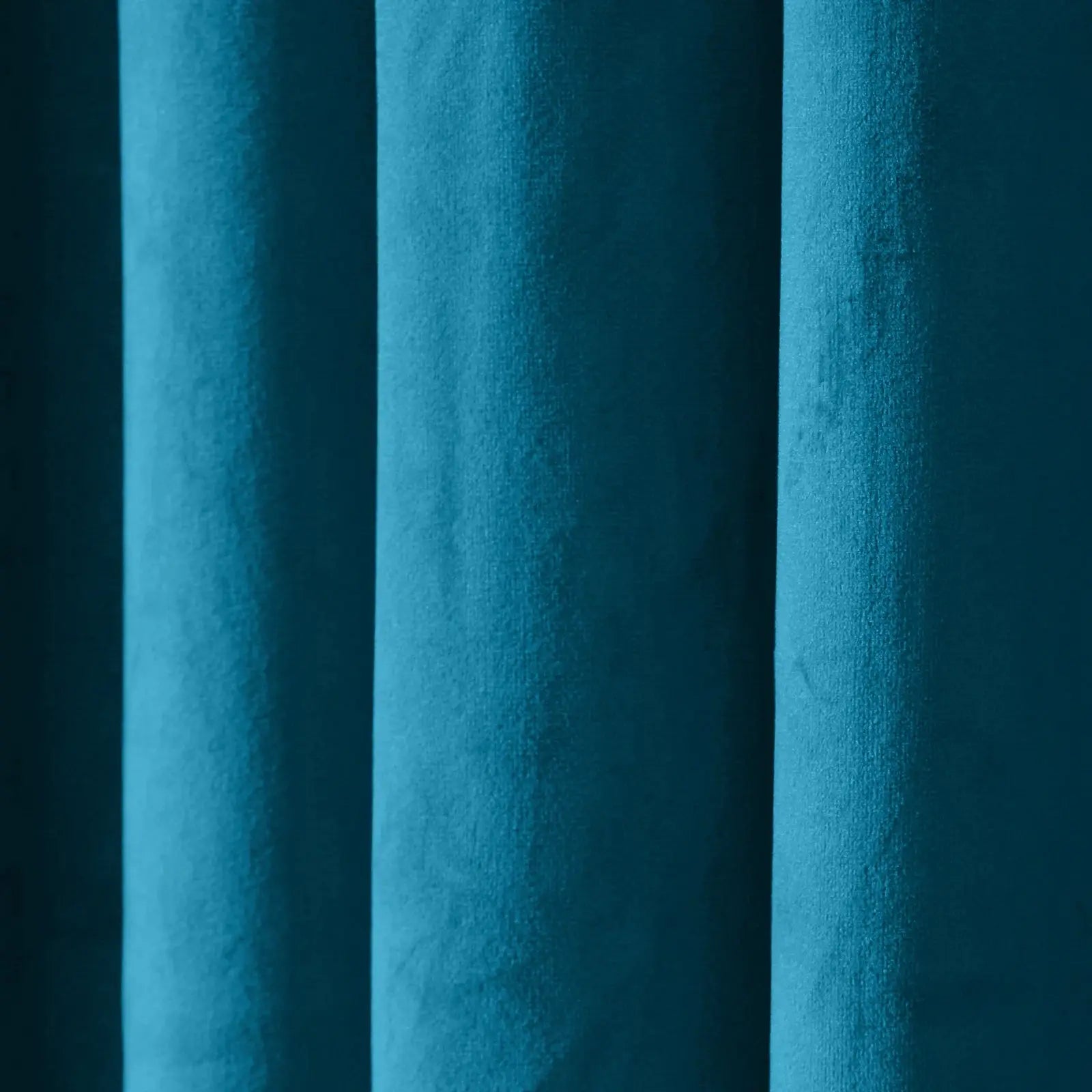 Close-up photograph of lush teal velvet fabric in deep vertical folds catching varied light