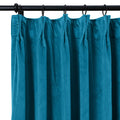 Teal velvet pleated curtain hanging on a black curtain rod with rings
